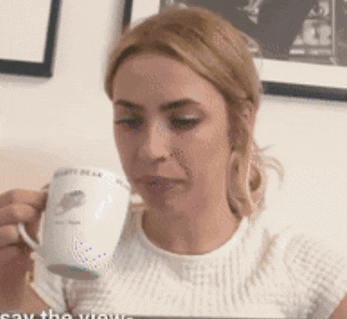 a woman in a white shirt is drinking from a white mug with a bird on it ..