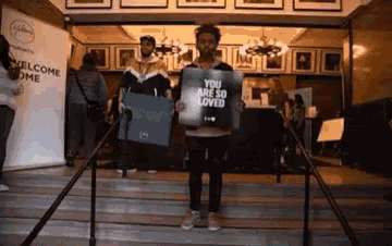 a man is holding a sign that says `` you are so loved '' while standing on stairs .