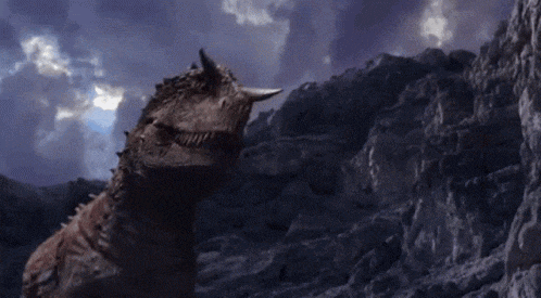 a dinosaur with horns is standing on a rocky hillside .