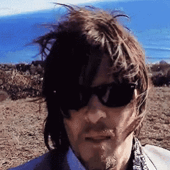 a man wearing sunglasses is standing in a field with a blue sky in the background .