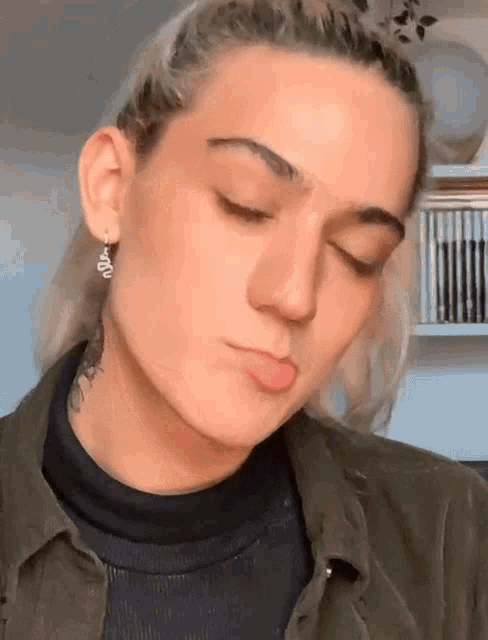 a woman wearing a green shirt and black turtleneck is making a face