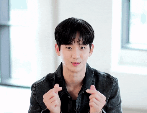 a young man in a denim jacket is making a heart with his hands .