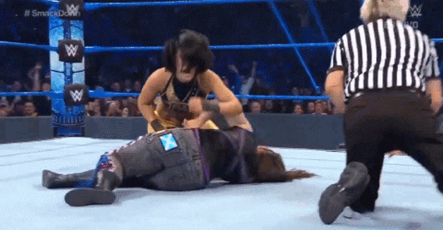 two women are wrestling in a wrestling ring with a referee watching .