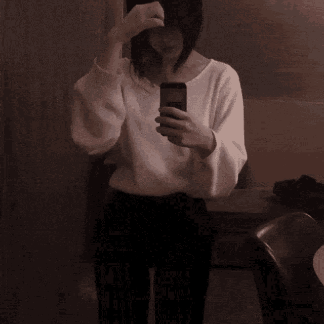 a woman in a white sweater is taking a picture of herself in the mirror