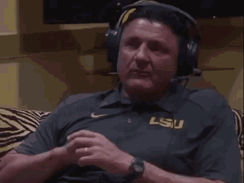 a man wearing headphones and a shirt that says lsu is sitting on a zebra print couch .