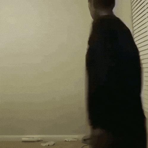a man in a black shirt is standing in a room with a window .