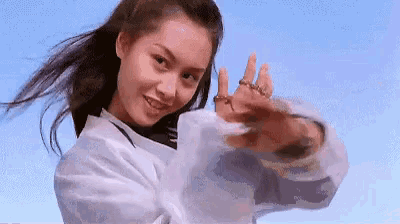 a woman in a white shirt is standing in front of a blue sky with her hands in the air .