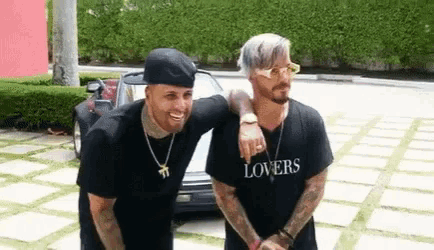 two men are posing for a picture in front of a car . one of the men is wearing sunglasses .