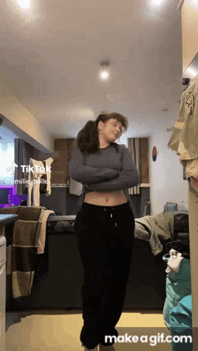 a woman is standing in a room with her arms crossed and a tiktok icon on the bottom right