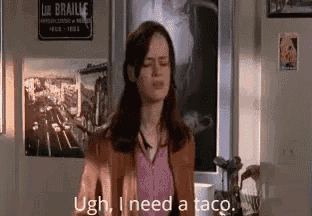 a woman is standing in front of a wall with a sign that says `` ugh , i need a taco ''