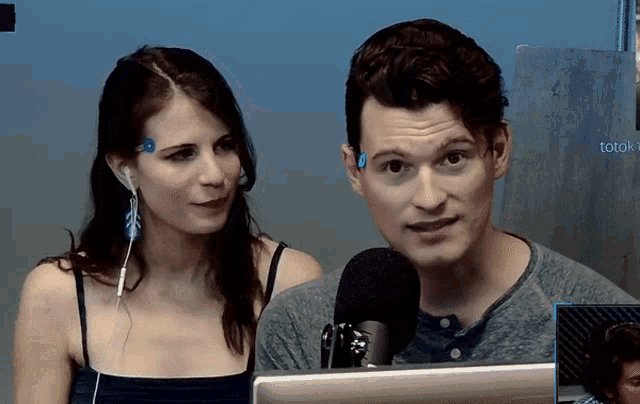 a man and a woman are sitting in front of a microphone with a screen that says totok on it