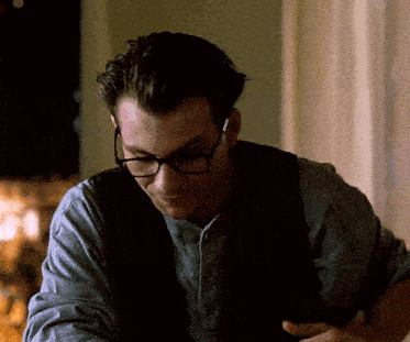 a man wearing glasses and a vest is looking down at something
