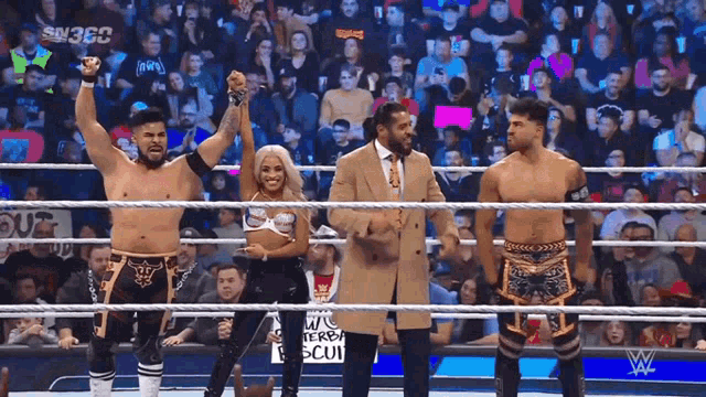 a group of wrestlers are standing in a wrestling ring with a man in a suit .