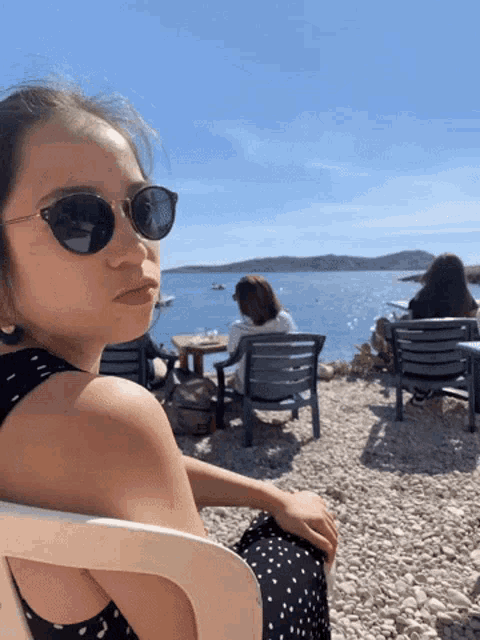 a woman wearing sunglasses sits in a chair near the ocean