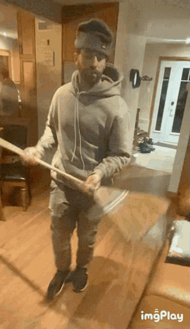 a man in a grey hoodie is holding a broom in his hands