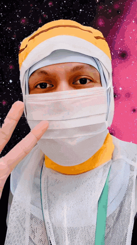 a person wearing a surgical mask and a yellow hat giving a peace sign