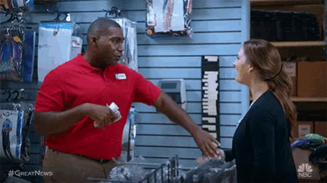 a man in a red shirt is talking to a woman in a store while holding a piece of paper .