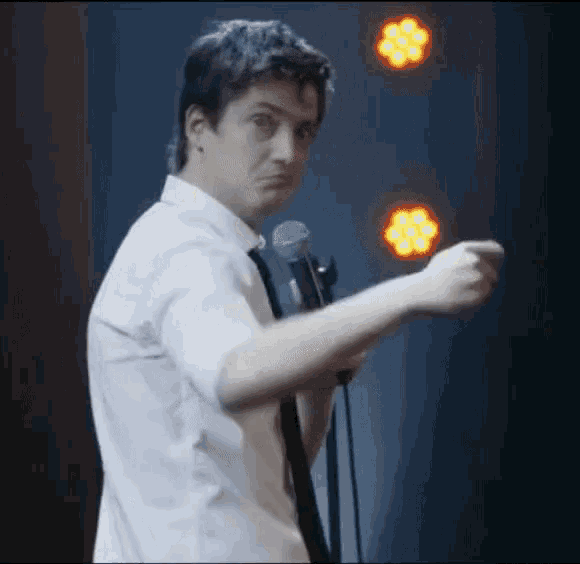 a man in a white shirt and tie is holding a microphone and pointing at something