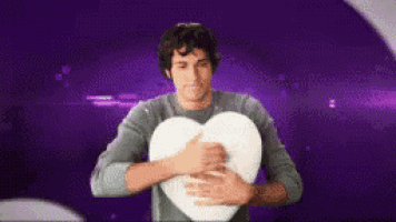 a man is hugging a heart shaped pillow against a purple background