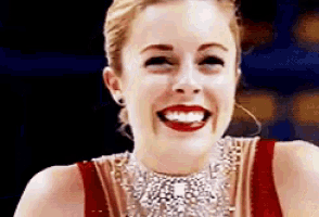 a woman wearing a red dress and a necklace is smiling with red lipstick .