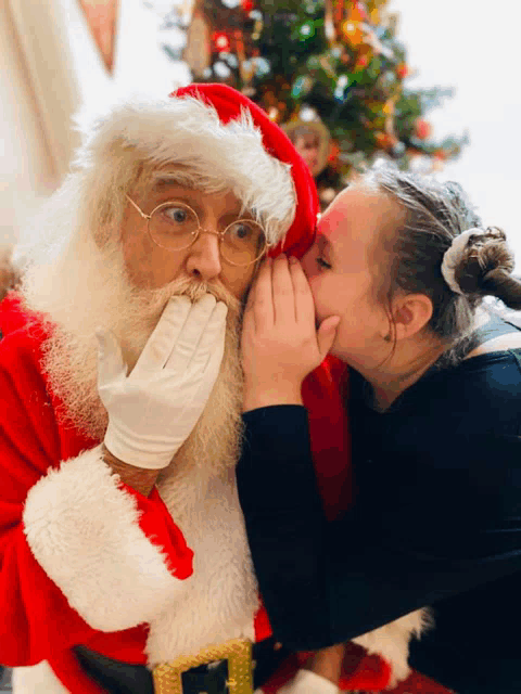 a little girl whispering into santa 's ear