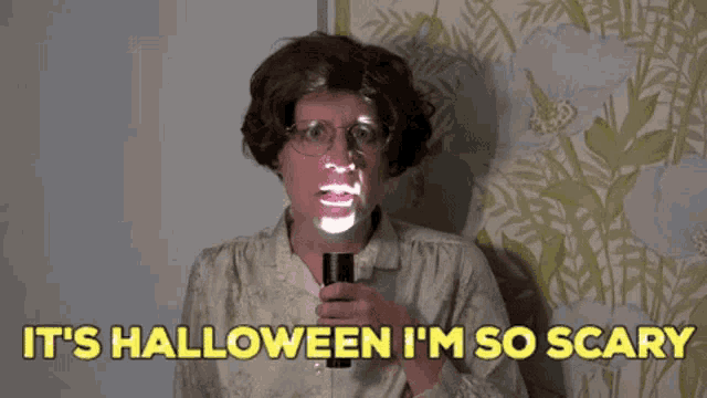 a woman with glasses is holding a flashlight and saying it 's halloween i 'm so scary .