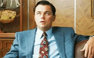 a man in a suit and tie is sitting on a couch with his hand on his knee .