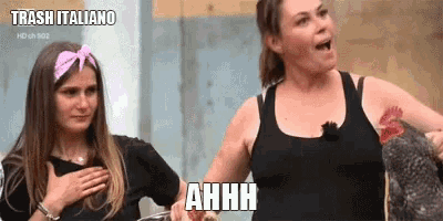 two women are standing next to each other and one of them is holding a chicken and the other is saying ahhh .