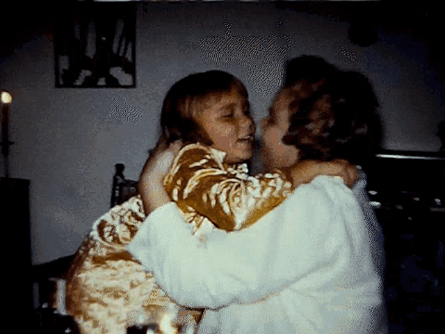 a woman in a white sweater is hugging a little girl in a brown and white dress