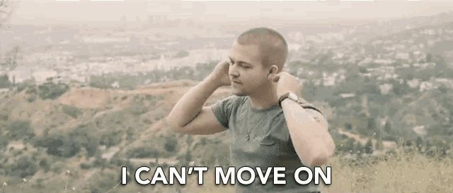a man is sitting on top of a hill with his hands behind his head and the words `` i can 't move on '' .