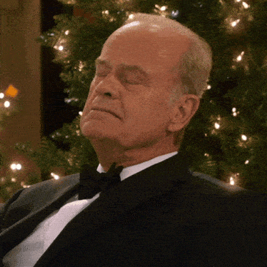 a man in a tuxedo is sitting in front of a christmas tree with his eyes closed