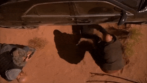 a man is standing under a car in the desert .