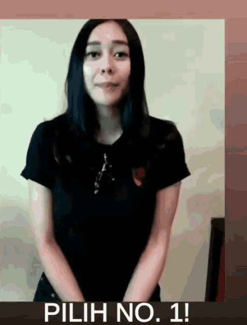 a woman in a black shirt stands in front of a sign that says " pilih no. 1 "