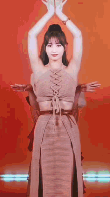 a woman in a lace up crop top and skirt is dancing with her arms in the air .