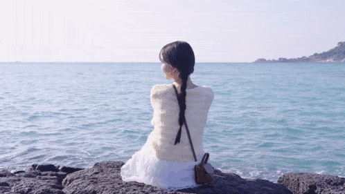 a woman sitting on a rock near the ocean
