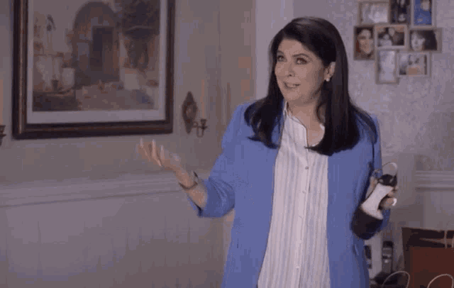 a woman in a blue jacket is standing in a living room with a picture on the wall .