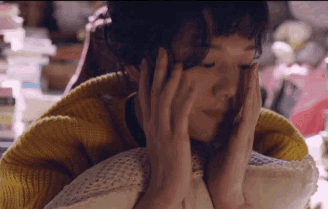 a woman in a yellow sweater is holding her head with her hands