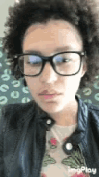 a woman wearing glasses and a jacket is making a face .