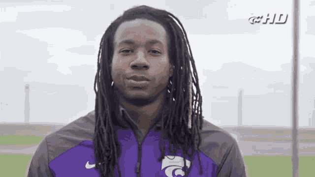 a man with dreadlocks is wearing a purple nike jacket and looking at the camera .