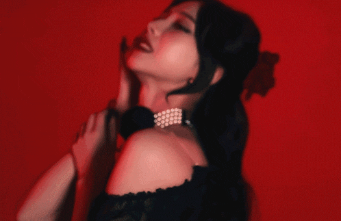 a woman in a black dress with pearls on her neck is standing in front of a red background