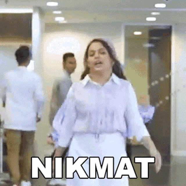 a woman in a purple shirt and white shorts is standing in a hallway with the word nikmat above her