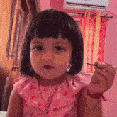 a little girl in a pink dress is holding a pencil in her hand .