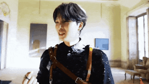 a young man wearing a black sweater and a brown leather harness is standing in a living room .