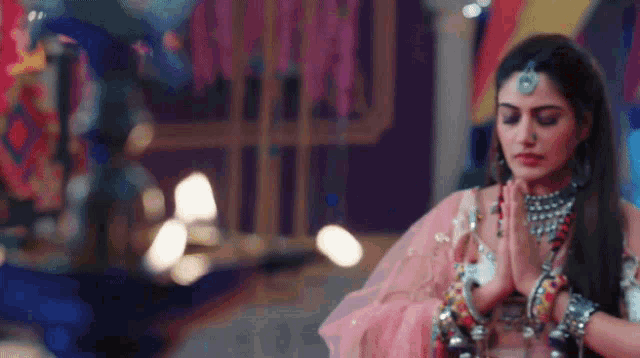 a woman in a pink dress and jewelry is praying with her hands folded .