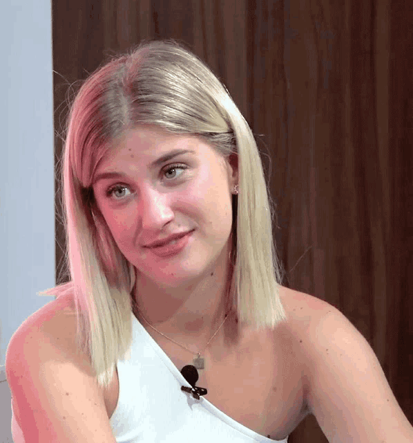 a blonde woman wearing a white one shoulder top and a necklace with a skull on it