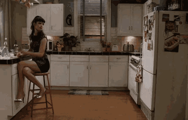 a woman sits on a stool in a kitchen with a bottle of wine on the counter