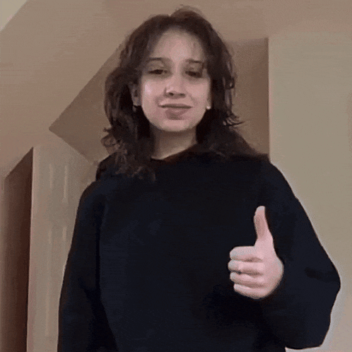 a young woman is giving a thumbs up sign while wearing a black sweater .