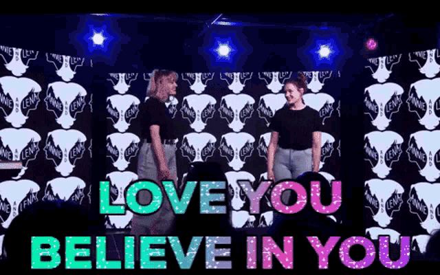 two women are dancing in front of a wall that says love you believe in you
