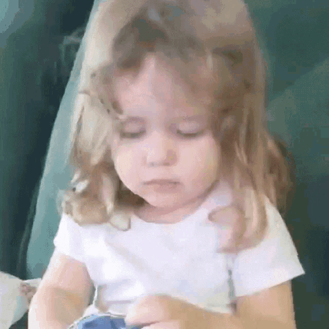 a little girl with long blonde hair is sitting on a couch with her eyes closed