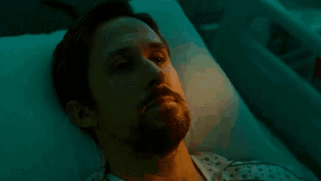 a man with a beard and mustache is laying in a hospital bed with his mouth open .
